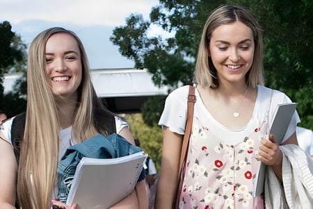 Dos estudiantes del Newstead College caminan sonriendo por el campus llevando libros y carpetas.