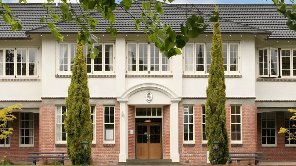 El edificio de ladrillo de la Nga Tawa Diocesan School con ventanas arqueadas y cipreses en primer plano.