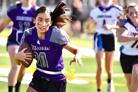 Una estudiante de Norfolk Christian Schools corre con un balón en el campo de deportes y está rodeada de otros jugadores.
