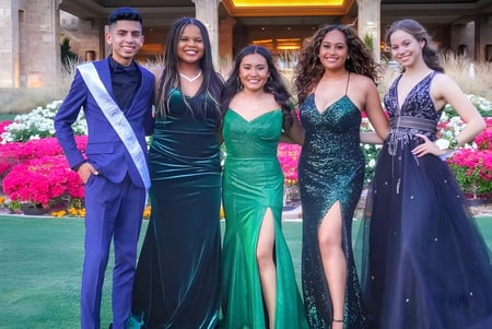 Cinco personas en ropa formal posan juntas en un área exterior llena de flores de la North Canyon High School.