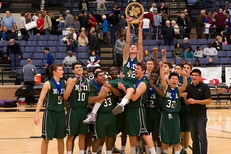 Un grupo de jugadores de baloncesto en camisetas verdes celebra en la cancha de la North Central Texas Academy frente a espectadores.