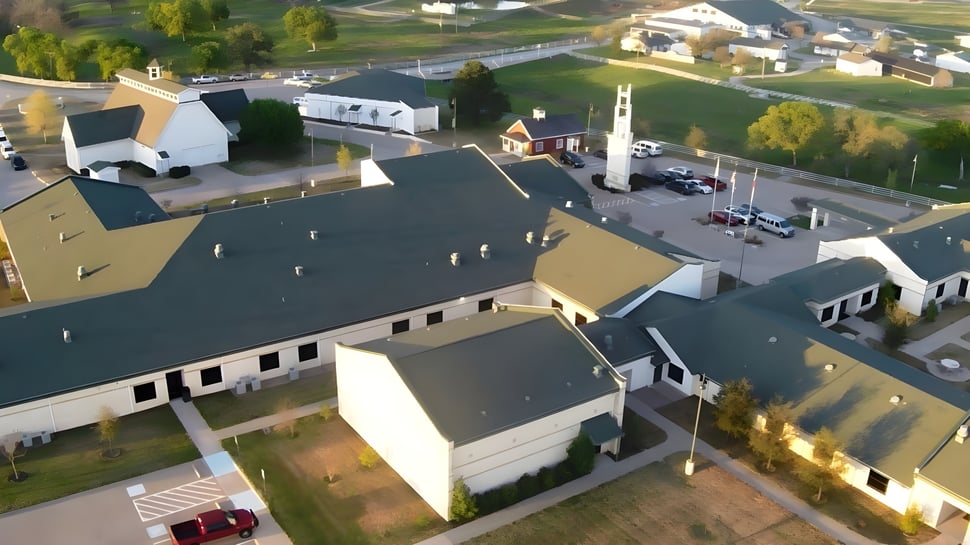 Vista del edificio principal y el entorno de la North Central Texas Academy con casas residenciales y mucho verde.
