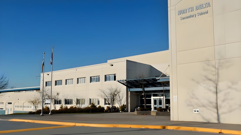 El moderno edificio de varios pisos de la North Delta Secondary School con un letrero visible bajo un cielo azul y un estacionamiento en primer plano.