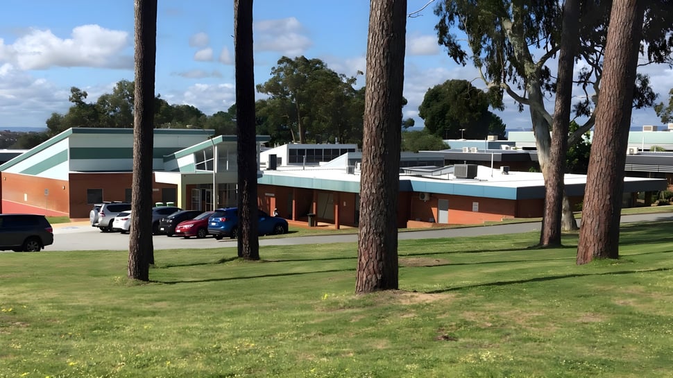 El moderno edificio de varios pisos con techo verde y pared exterior de ladrillo en el campus de North Lake Senior Campus rodeado de pinos.