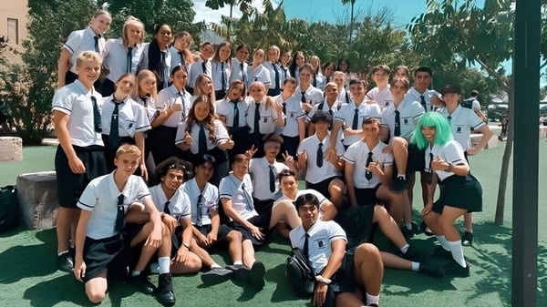 Un grupo de estudiantes se reúne en un campo con palmeras en el campus de North Lakes State College.