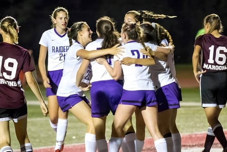 Un grupo de atletas femeninas de la North Shore Country Day School se reúne por la noche en el campo deportivo.