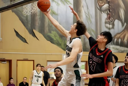 Dos jugadores de baloncesto luchan por el balón frente a un mural de bosque en el terreno de la North Surrey Secondary School.