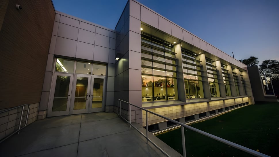 El moderno edificio de varios pisos de la Northeastern Wisconsin Lutheran High School con paredes de vidrio está iluminado en un área de césped.