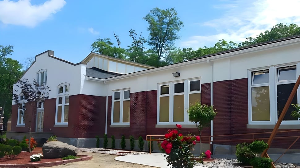 El moderno edificio de ladrillo y pintado de blanco de la Northern Academy con grandes ventanas y un patio verde bajo un cielo azul.