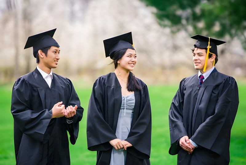 Tres graduadas y graduados de la Northern Academy están al aire libre en un campo con sus togas de graduación.