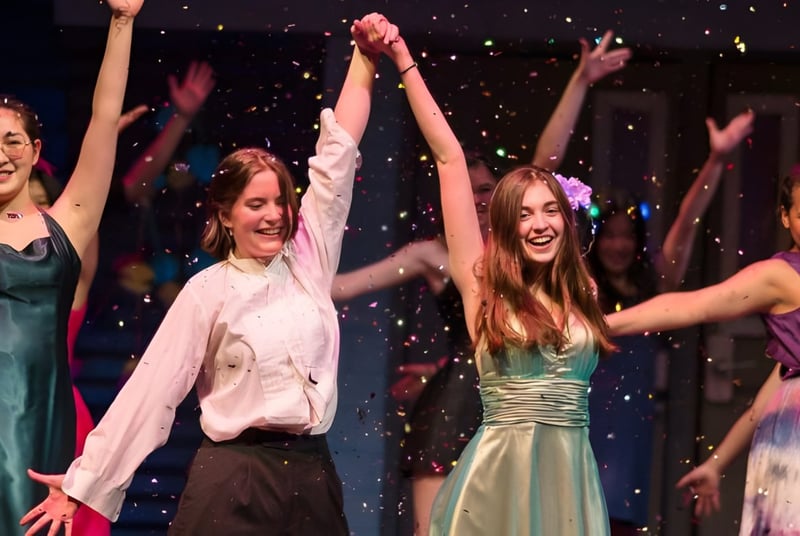 Un grupo de jóvenes mujeres baila en el escenario de la Northfield Mount Hermon School frente a un fondo brillante.