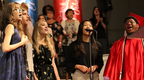 Estudiantes de la Northside Christian Academy se presentan en un escenario con cortina roja y cantan juntos.