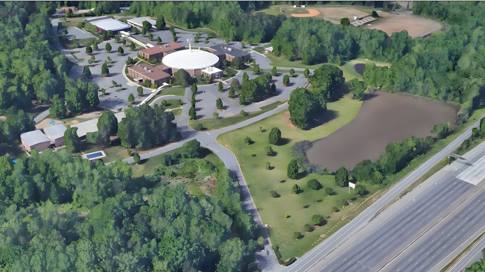 El campus de la Northside Christian Academy muestra un gran edificio en forma de cúpula en un paisaje boscoso cerca de un cuerpo de agua.