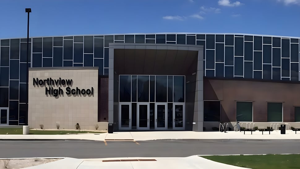 El moderno edificio escolar de varios pisos de la Northview High School con fachada de azulejos negros y grises está rodeado de una superficie de césped y un camino pavimentado.
