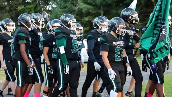 Un grupo de jugadores de fútbol de Northwest Catholic High School está junto frente a un fondo verde de árboles y plantas.