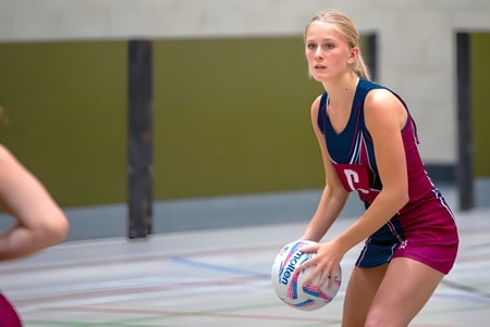 Una estudiante de la Norwich School sostiene un voleibol en el campo deportivo con una pared verde de fondo.