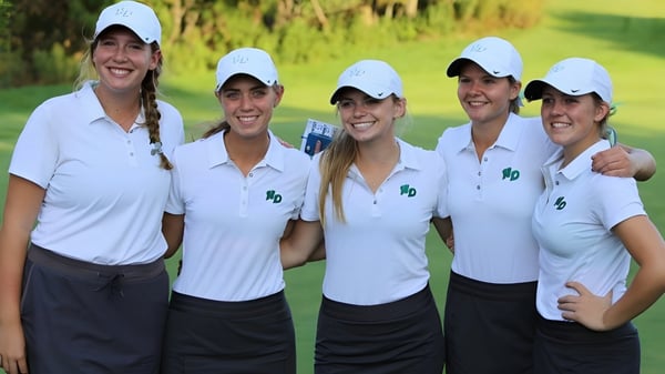 Un grupo de cinco estudiantes en camisetas blancas de golf está de pie en un campo de césped en el campus de la Notre Dame de la Baie Academy.