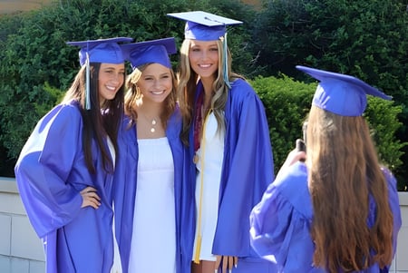 Cuatro estudiantes de la Notre Dame de la Baie Academy en togas de graduación están juntas frente a un fondo verde.