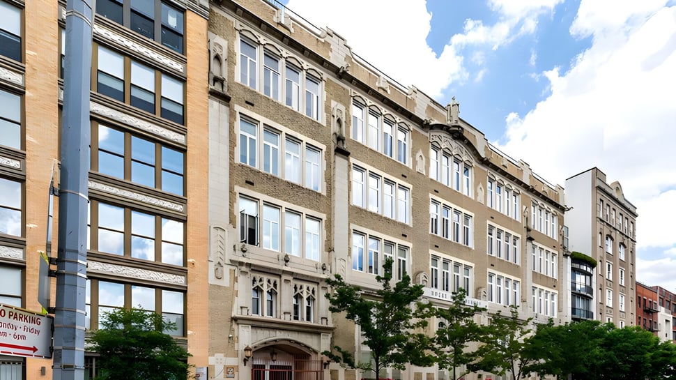 El edificio de ladrillo de Notre Dame High School muestra una arquitectura de varios pisos con muchas ventanas y adornos bajo un cielo azul.