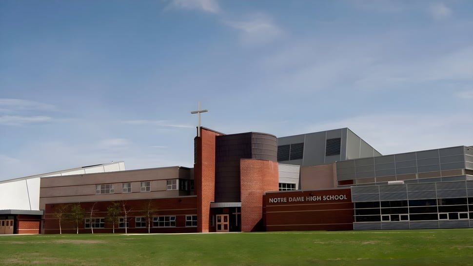 El moderno edificio escolar de la Notre Dame High School en Calgary con fachada de ladrillo y grandes ventanas bajo un cielo despejado.