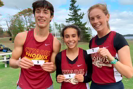 Tres personas en uniformes deportivos de Citadel Phoenix posan juntas frente a un paisaje con árboles y agua en Nova Scotia.