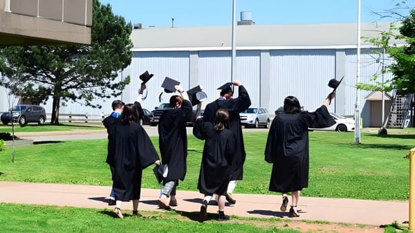 Un grupo de graduados en togas negras camina por el campus de la Nova Scotia School sobre un prado frente a un gran edificio.
