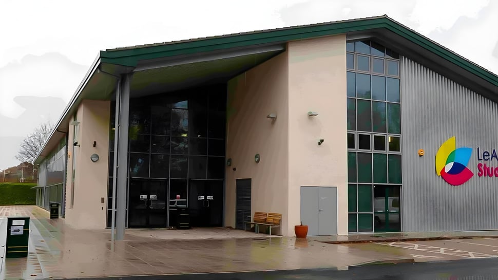 El moderno edificio de varios pisos del Oak Leaf Studio con techo verde y grandes ventanales de vidrio está rodeado de un área pavimentada.