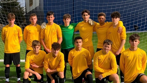 Un grupo de jóvenes futbolistas en camisetas amarillas posan frente a una red azul en el campo deportivo del Oak Leaf Studio.