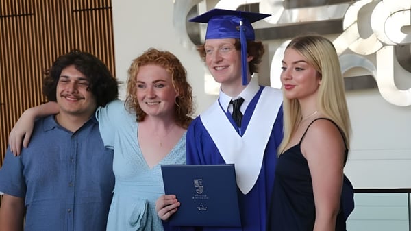 Cuatro personas, incluyendo a un graduado en toga, están juntas en una ceremonia de graduación de la École Secondaire Oak Park High School.