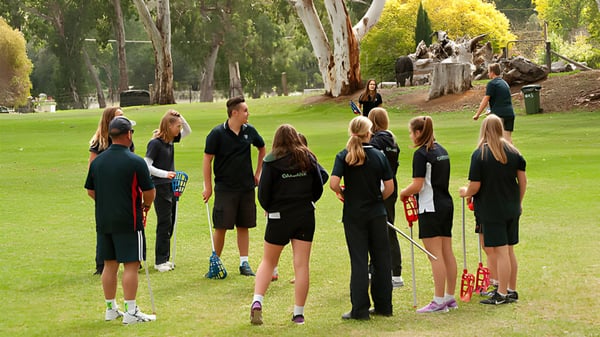 Un grupo de alumnas y alumnos de la Oakbank Area School está en un campo verde rodeado de árboles.