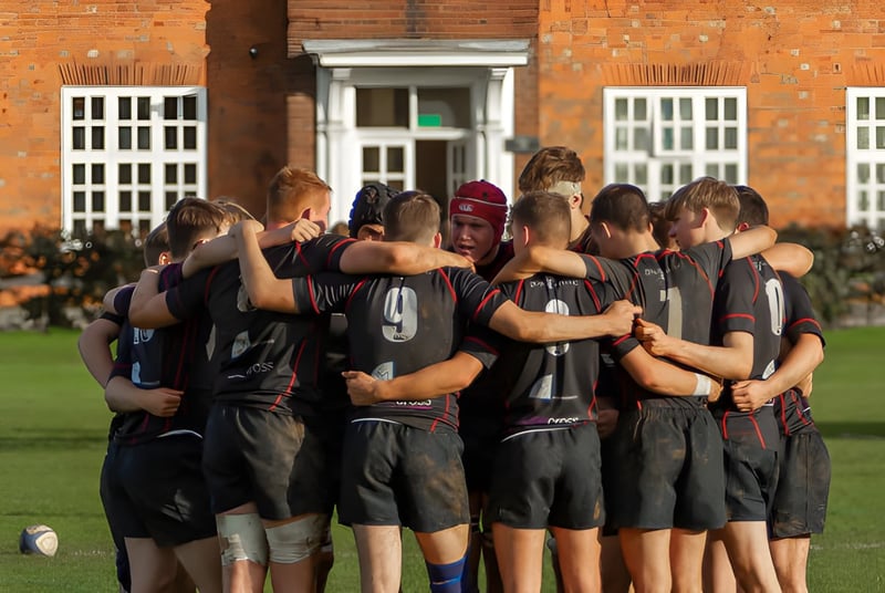 Un grupo de estudiantes de la Oakham School está en uniformes deportivos frente a un edificio de ladrillo.