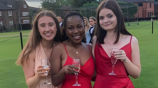 Tres estudiantes de la Oakham School están en un campo de césped sosteniendo copas de champán.