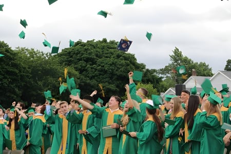 Un gran grupo de graduados en túnicas verdes y amarillas está al aire libre en el terreno de Oakland Christian School.