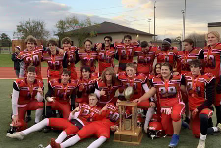 Un grupo de jóvenes futbolistas de la Oakville Trafalgar High School posan con un trofeo en un campo de deportes.