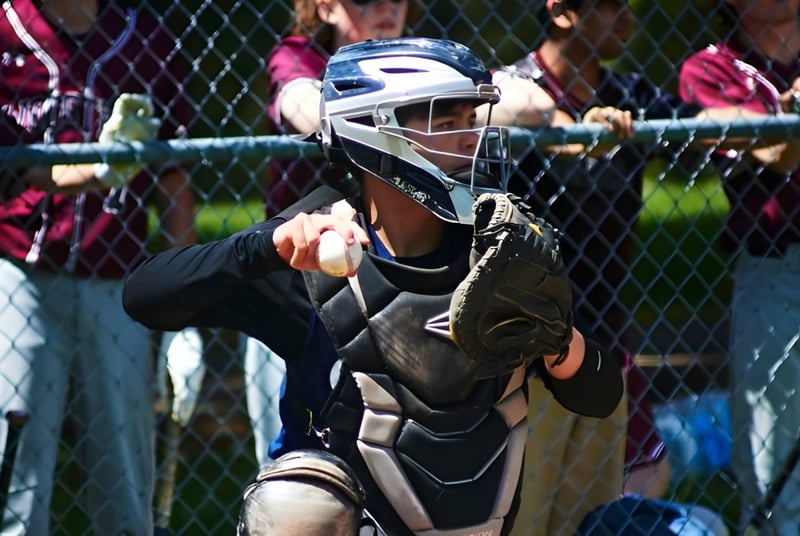 Una persona con una máscara de catcher de béisbol está de pie detrás de una cerca de alambre en el terreno de la Oakwood Friends School.