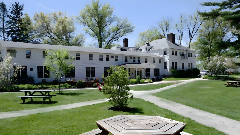 El edificio blanco de varios pisos de la Oakwood Friends School está rodeado de un césped con árboles y un camino pavimentado.