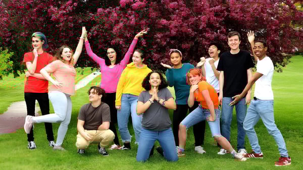 Un grupo de estudiantes de la Oakwood Friends School está de pie en un campo frente a árboles rosados en flor.