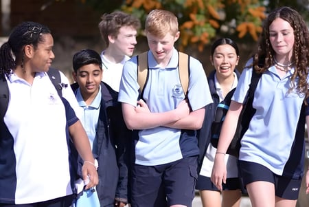 Un grupo de estudiantes de la Ocean Reef Senior High School está juntos afuera frente a un follaje otoñal.