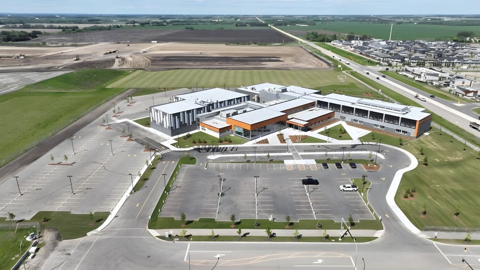 El moderno edificio de la Ohpaho Secondary School está rodeado de campos y una calle con un estacionamiento adyacente.