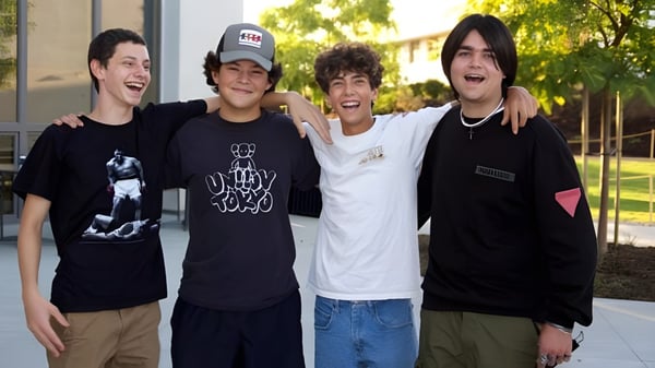 Cuatro estudiantes de la Ojai Valley School están juntos al aire libre sonriendo frente a un edificio con árboles.
