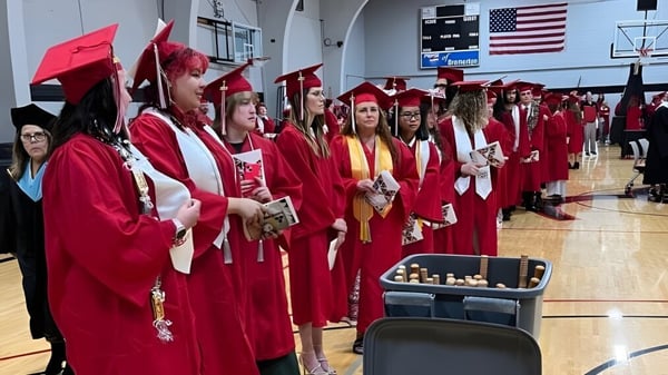 Graduados y graduadas en togas rojas están en el gimnasio del Olympic College.