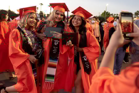 Un grupo de graduados en togas rojas sostiene sus diplomas al aire libre en las Orange County Public Schools.