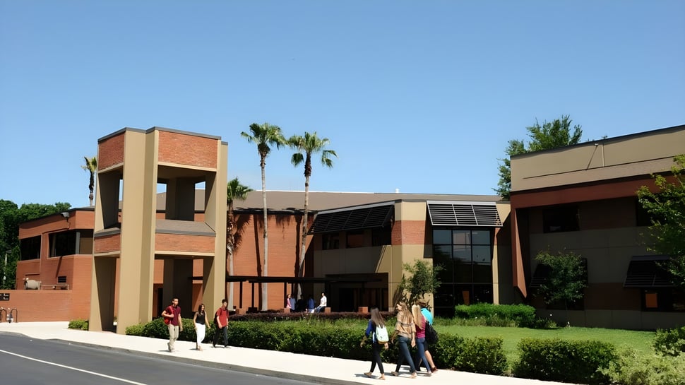 El moderno edificio de ladrillo de la Orangewood Christian School con palmeras y personas en primer plano.