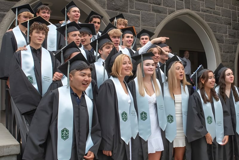 Un grupo de graduados en togas se encuentra frente a un edificio de piedra en el campus de la Oregon Episcopal School.