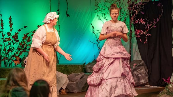 Dos mujeres en vestidos coloridos están en el escenario de la Oregon Episcopal School frente a un fondo floral.
