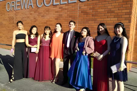 Un grupo de estudiantes está frente al edificio de ladrillo del Orewa College.