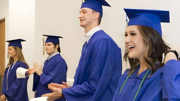 Un grupo de graduadas y graduados de la Ormeau Woods State High School está juntos en el pasillo con ropa azul y birretes.