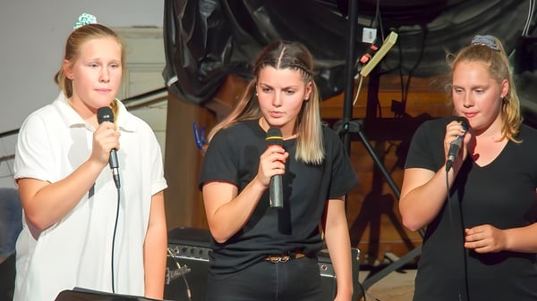 Tres estudiantes de la Orroroo Area School cantan juntas en micrófonos en el escenario.