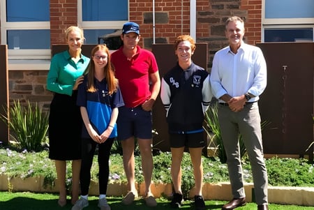 Un grupo de cinco personas está frente al edificio de ladrillo con ventanas azules en el campus de la Orroroo Area School.