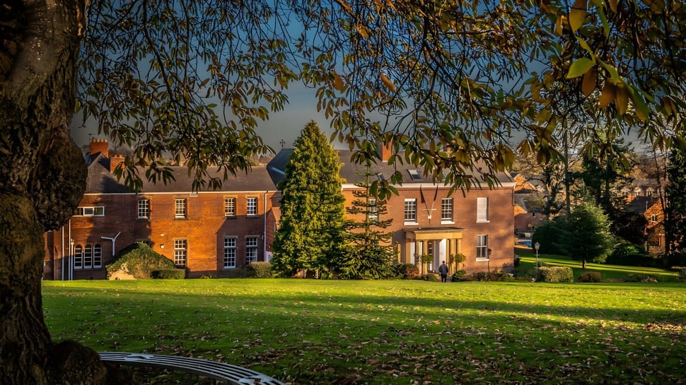 El edificio de ladrillo de la Oswestry School está rodeado de un paisaje verde bajo un cielo azul claro.